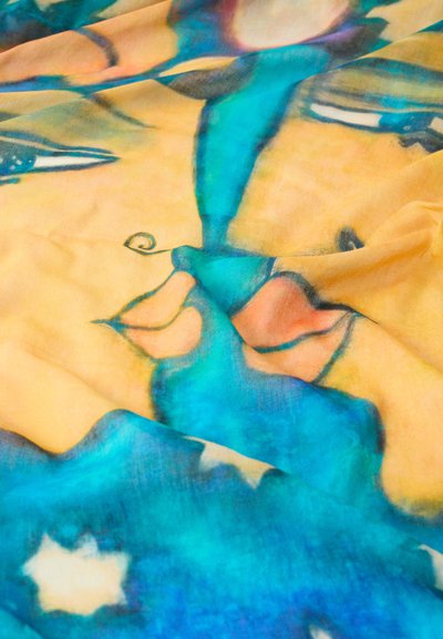 Écharpe en soie colorée présentant des motifs abstraits de visages en nuances d'orange, bleu et jaune, avec une texture douce et un tissu fluide.
