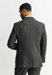 Blazer de lana gris oscuro con un acabado texturizado, una abertura en la parte posterior y solapas de muesca, combinado con pantalones a juego.