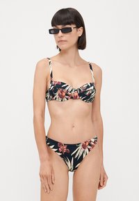 Cvetni bikini iz temnega blaga; zgornji del z nabranim sprednjim delom, nastavljive naramnice. Spodnji del ima podoben cvetlični vzorec, srednja pokritost.