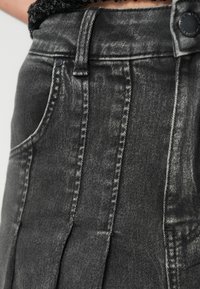 Saia de ganga cinza com cintura alta, costura detalhada, design plissado e bolsos laterais. Material texturizado com um visual desgastado.