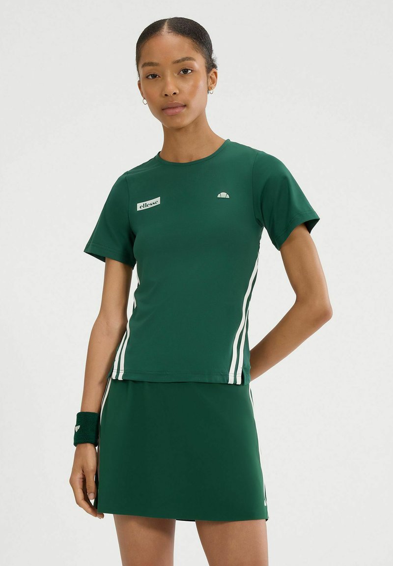Zielony zestaw sportowy składający się z topu i spódnicy, wykonany z gładkiego, elastycznego materiału. Posiada białe paski po bokach oraz małe logo na klatce piersiowej.