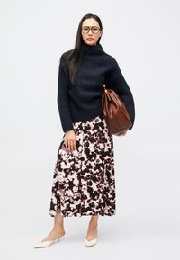 Μπλε σκούρο ριγωτό πουλόβερ με ψηλό λαιμό, φλοράλ φούστα σε αποχρώσεις του ροζ και κρέμ, καφέ δερμάτινη τσάντα, κρεμ παντόφλες, μαύρα γυαλιά με χοντρό σκελετό.