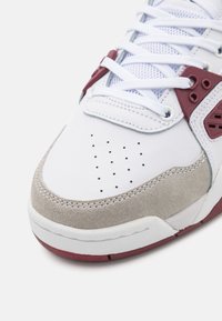 Baskets blanches et bordeaux avec embout perforé, surcouche en daim beige, lacets blancs et détail de languette en tissu mesh.