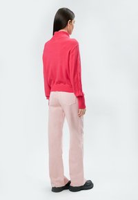 Pull en maille fuchsia avec un col montant et des détails en tricot torsadé, associé à un pantalon large rose clair et des chaussures à plateforme noires épaisses.