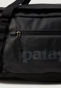 Nærbillede af en sort vandtæt Patagonia duffelbag med lynlås lomme og justerbar skulderrem.