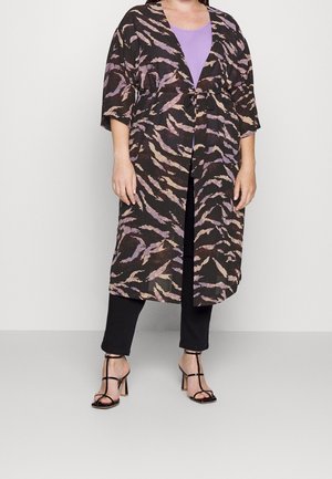 Persoon draagt zwarte cropped broek, zwarte sandalen met bandjes, paarse top en doorschijnende zwarte en paarse patroon lange kimono-achtige cardigan.