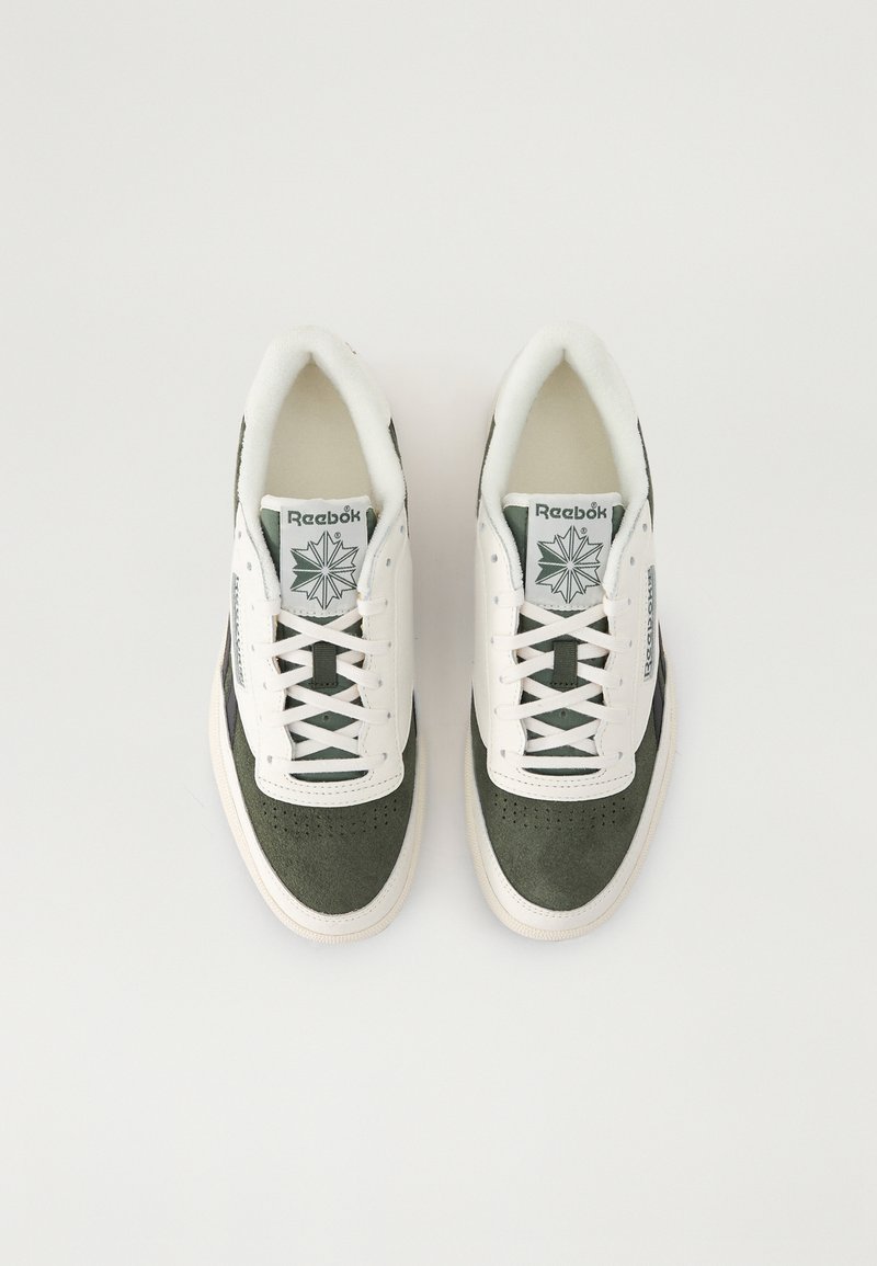 Baskets vertes et blanches en matériaux daim et cuir, avec un bout perforé, des lacets plats et un logo sur la languette et le côté.