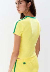 Geel katoenen T-shirt met groene accenten op de mouwen en kraag, voorzien van een getailleerd ontwerp en een cropped lengte.