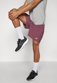 Idrettsantrekk bestående av en grå skjorte, maroon shorts og svarte joggesko med hvite såler. Sokkene er hvite og knelange.