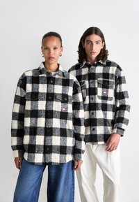 Sort og hvid ternet flannel skjorter med knaplukninger, forlommer og kontrasterende teksturerede firkanter; båret med denim- og elfenbenbukser.
