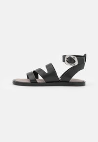 Sandal in pelle nera con molteplici cinturini larghi, fibbia alla caviglia, suola piatta e cuciture a contrasto lungo il bordo. Design minimalista.