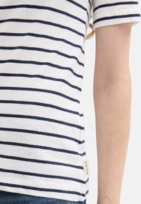 Bomulds t-shirt med marineblå vandrette striber på hvid baggrund. Korte ærmer og et sideetiket med brandnavnet. Blød tekstur.