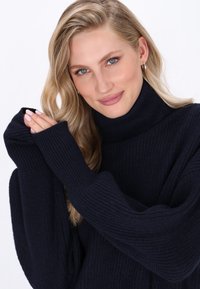 Maglione a collo alto oversize di colore blu navy realizzato in tessuto a coste, con maniche ampie e una vestibilità comoda e rilassata.