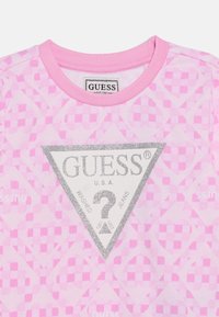 Ροζ βαμβακερό μπλουζάκι με επαναλαμβανόμενο καρό μοτίβο, ασημένιο τριγωνικό λογότυπο με την επιγραφή "GUESS U.S.A." και στρογγυλή λαιμόκοψη.