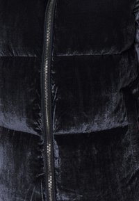 Giacca puffer di un blu navy scuro con una texture morbida e vellutata. Presenta una chiusura centrale in metallo argentato e sezioni imbottite per l'isolamento.