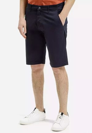 Granatowe bawełniane szorty z szlufkami na pasek i kieszeniami bocznymi, charakteryzujące się dopasowanym krojem i podwiniętymi brzegami, w połączeniu z białymi trampkami.