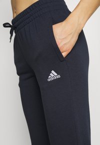 Joggers en color marino con tejido texturizado, cintura elástica y cordón ajustable. Presentan bolsillos laterales y el logo blanco de Adidas en el muslo.