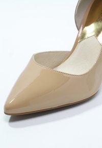 Escarpin en cuir verni beige avec un bout pointu et un design dégagé. Texture lisse avec un léger éclat, doté d'une doublure intérieure beige.