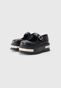 Black platform Mary Jane shoes with thick soles featuring metallic silver accents and buckle straps on a white background.