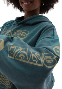 Felpa teal con grafica in oro lungo le maniche. Materiale in cotone, vestibilità comoda e cappuccio con lacci. Texture morbida e design casual.