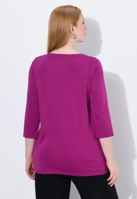 Fuchsia 3/4 mouw top met een ronde halslijn, gemaakt van gladde stof. Achteraan is het een eenvoudig ontwerp zonder versieringen of patronen.
