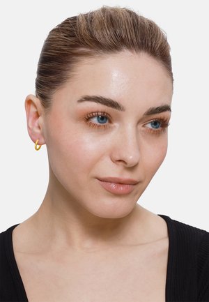 Boucle d'oreille en or présentée sur un modèle. Texture lisse, forme circulaire, design léger et finition polie qui complète le teint de la peau.