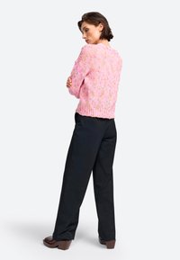 Pull en tricot rose avec une coupe décontractée, motif texturé et ourlet côtelé, associé à un pantalon noir taille haute et des chaussures à talons épais marron.