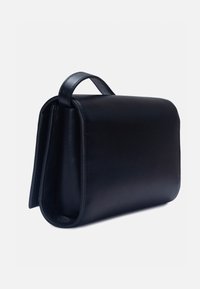 Sac à main rectangulaire en cuir noir avec une fermeture à rabat et une courte poignée sur le dessus, présenté sous un léger angle sur un fond blanc.