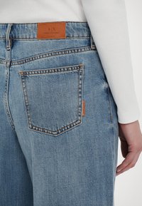 Svetlo modri trijezni jeans z ravnim krojem. Imajo usnjen označevalni znak na zadnjem pasu in šive kot dekoracijo na žepih.