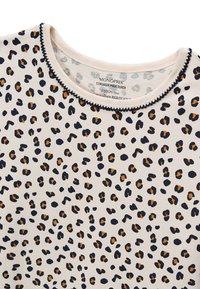 Chemise en coton avec une base beige ornée d'un imprimé léopard noir et marron, finition avec un col noir cousu.