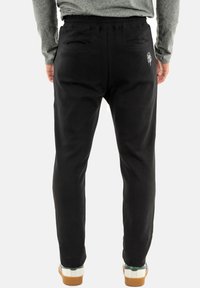 Pantaloni da jogger neri realizzati in tessuto leggero, con vita elasticizzata, due tasche posteriori e un logo grafico bianco sul lato destro.