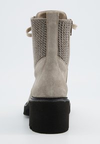 Bottine en suède beige avec panneaux en tissu texturé. Talon carré, fermeture éclair et languette arrière pour un enfilage facile. Semelle en caoutchouc pour une meilleure adhérence.