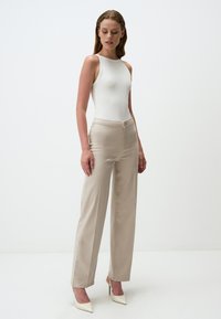 Body bianco senza maniche abbinato a pantaloni ampi beige e tacchi a punta bianchi. Tessuto morbido, vita alta e chiusura con bottone anteriore.