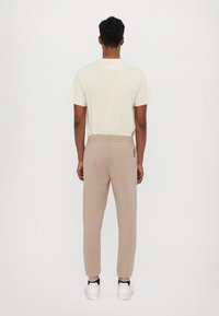 Beige katoen T-shirt met een klein logo op de achterkant, gecombineerd met beige joggingbroeken met een elastische tailleband en zijaccentdetails.