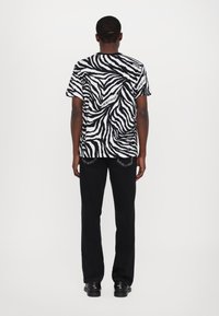 Svart-hvitt zebra-stripet t-skjorte med avslappet passform, parret med svarte bukser og elegante svarte sko. Designet for hverdagsbruk.