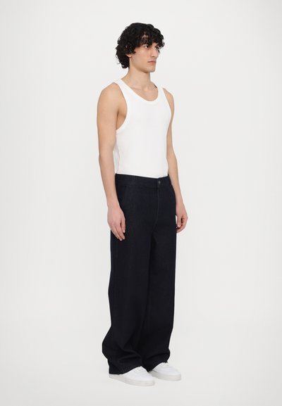 White tank top paired with loose-fitting dark denim trousers. The outfit features a classic design with a smooth texture and a button closure.