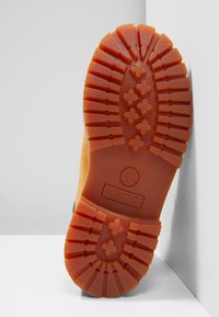Suola degli stivali Timberland, in gomma marrone con profondi motivi di battistrada e logo centrale. Superficie strutturata con elementi di trazione a motivo incrociato.