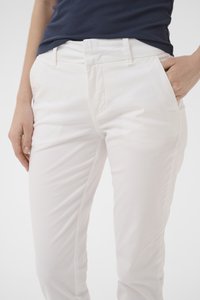 Persoană purtând pantaloni albi croiți și un top fără mâneci bleumarin cu model în relief, cu o mână în buzunar, decupată la nivelul taliei și coapselor.