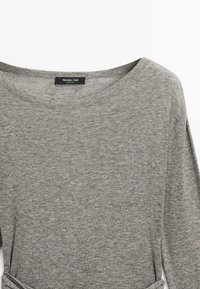 Szara koszula z długim rękawem wykonana z miękkiego materiału, z szerokim dekoltem i subtelną fakturą. Etykieta widoczna przy dekolcie. Casualowy design.