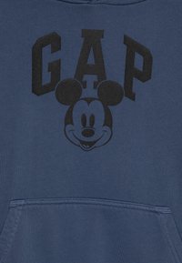 Tamno plavi dukserica s kengurú džepom, s crnim natpisom "GAP" i crnom grafikom Mickey Mouse-a u sredini. Mekana tekstura.