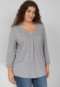 Szary longsleeve z dekoltem w kształcie litery V i detalem w postaci fałdy na środku. Miękka tekstura i luźny krój, w zestawieniu z dżinsami.
