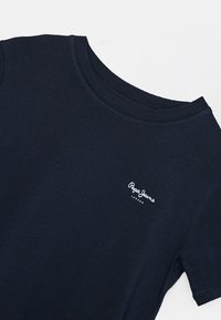 Námořnická modrá bavlněná tričko s krátkým rukávem, kulatým výstřihem a bílým vyšitým logem na přední straně. Měkká textura a jednoduchý design.