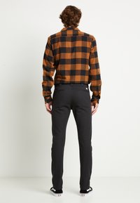 Ruskea ja musta ruudullinen flanellipaita pitkillä hihoilla, yhdistetty mustiin kapeisiin housuihin, päällä mustat ja valkoiset kengät.