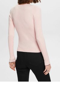 Haut à manches longues côtelé rose clair avec une coupe ajustée. Il présente un col rond et des poignets sombres contrastants, associé à un pantalon foncé.