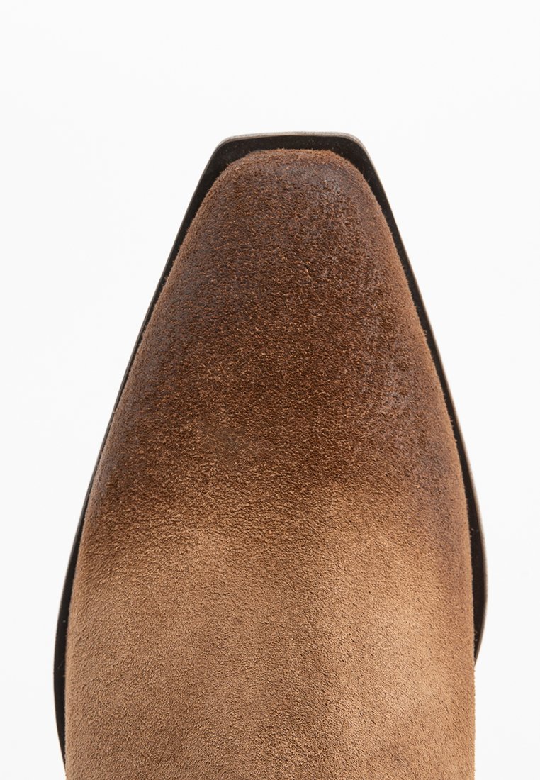 Zapato de ante marrón con un diseño de punta afilada, que presenta una textura suave y una suela delgada de cuero negro. Sin herrajes ni patrones visibles.