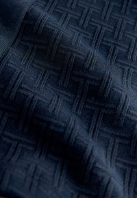 Donkerblauwe stof met een verhoogd geweven patroon in de vorm van onderling verbonden T-vormen, met zichtbare textuur en zachte plooien.