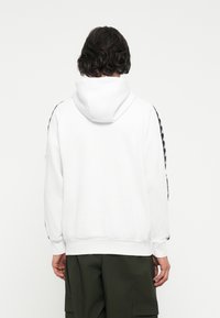 Sudadera blanca con capucha ajustable, presenta acentos laterales negros con un patrón geométrico, textura suave y puños y dobladillo acanalados.