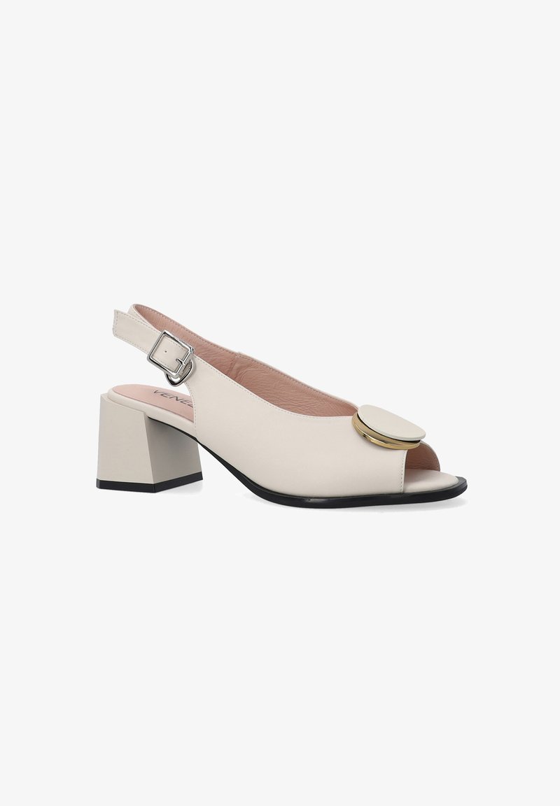 Cremefarvet slingback hæl med en peep-toe design, der har et stort cirkulært guldaccent og en firkantet blokhæl.