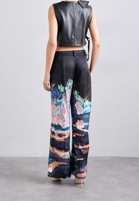 Haut court en cuir noir avec col, assorti à un pantalon large coloré présentant des motifs abstraits dans des tons de bleu, rose et noir.