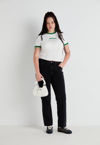 White cotton t-shirt with green trim, black straight-leg pants, white handbag, and multi-color sneakers. Simple design, casual fit.